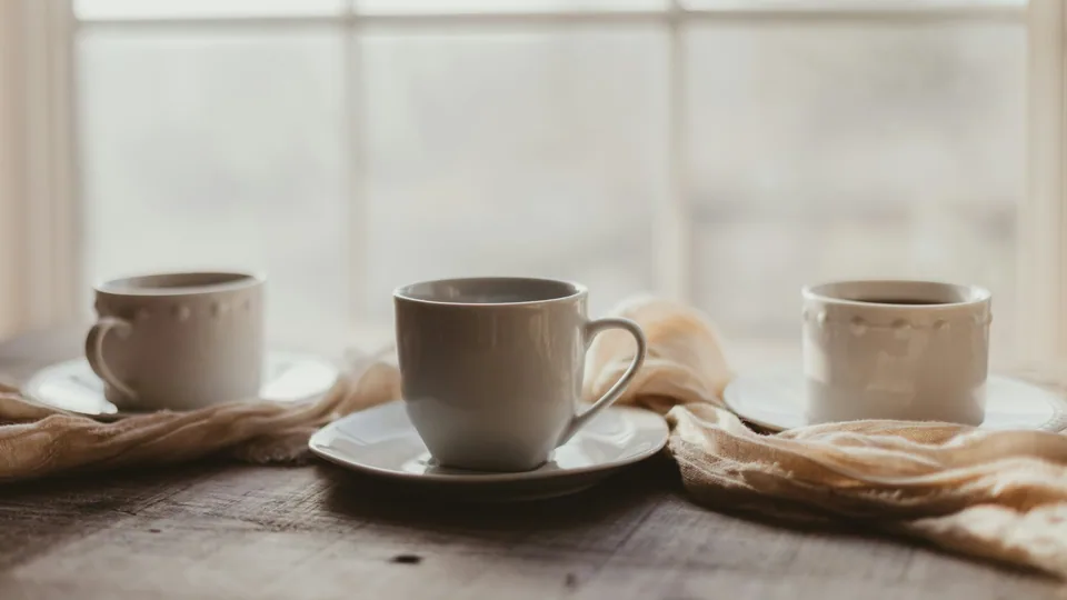 窓辺の木のテーブルに並ぶ3つの白いコーヒーカップ